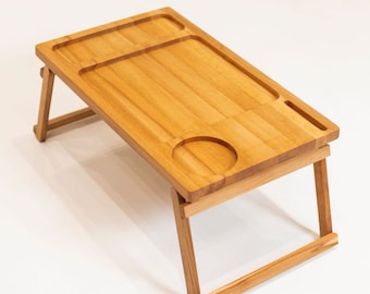May include: A wooden folding tray table with a built-in cup holder. The table is made of light brown wood and has a rectangular shape.
