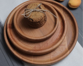 May include: Three wooden serving trays of varying sizes, stacked on top of each other. The trays are made of light brown wood and have a smooth, polished finish. A stack of cookies is sitting on the top tray.