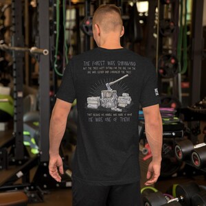 May include: A dark heather gray short-sleeve t-shirt featuring a graphic on the back of an axe embedded in a tree stump with stacks of wood. The text reads: The forest was shrinking but the trees kept voting for the axe, for the axe was clever and convinced the trees that because his handle was made of wood he was one of them.