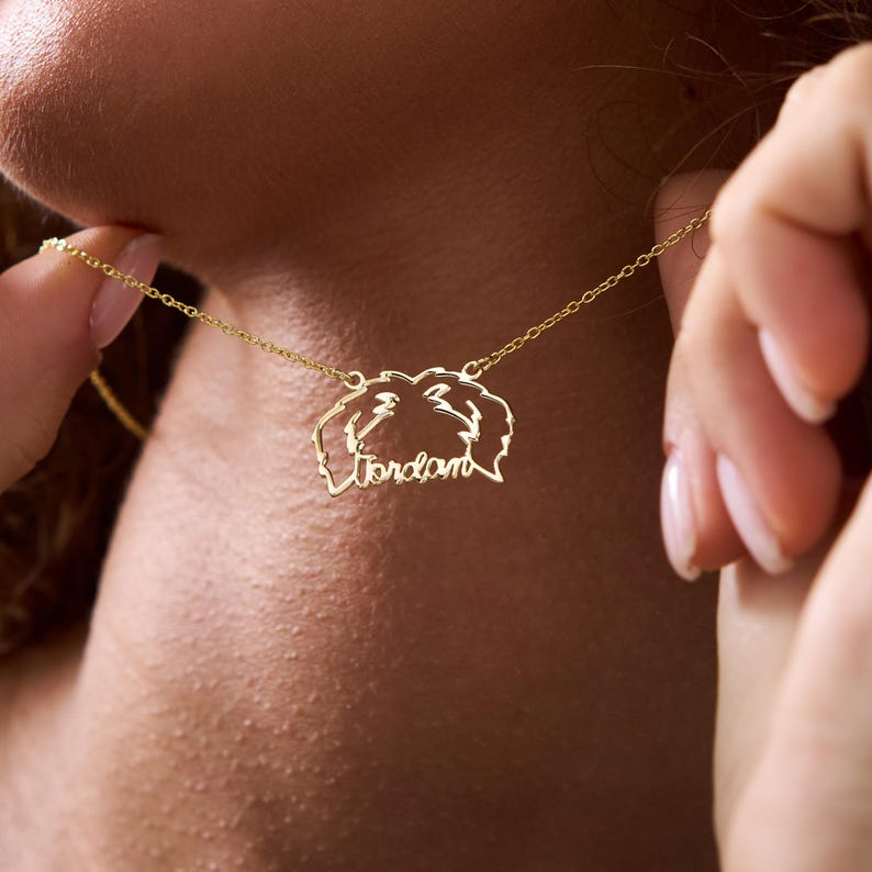 May include: A gold necklace with a pendant featuring a stylized outline of a dog's head with the name "Jordan" inscribed inside.