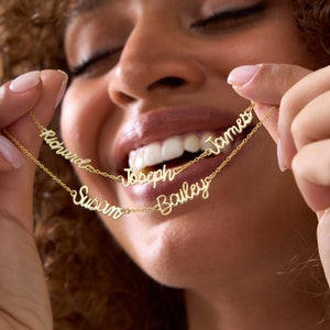 Puede incluir: Un collar de oro con cinco nombres: Richard, Joseph, Susan, Bailey y James. El collar está en capas y los nombres están escritos en una fuente cursiva.