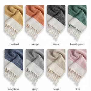 May include: A display of eight colorful woven towels, each folded to show a diamond pattern and white fringe. Colors include mustard, orange, black, forest green, navy blue, gray, beige, and pink. The text "Available Colors" is at the top.