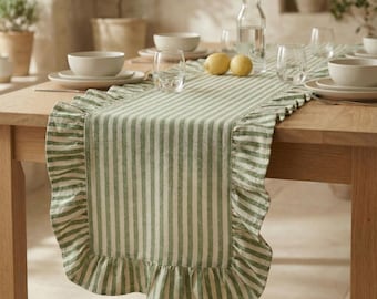 May include: A green and white striped table runner with a ruffled edge. The runner is placed on a wooden table, with white bowls, plates, and glasses visible. Two lemons are on the table.
