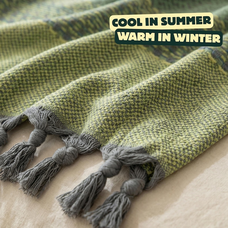 May include: Close-up of a woven blanket in shades of green and gray, with decorative tassels at the edge. The blanket has a textured appearance and the text "COOL IN SUMMER WARM IN WINTER".