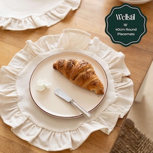 May include: Beige round placemat with a ruffled edge, a plate with a croissant, and a butter knife. The plate is on a wooden table. The placemat is 16 inches or 40cm in diameter. The text on the image says "Wellstil 16" 40cm Round Placemats."