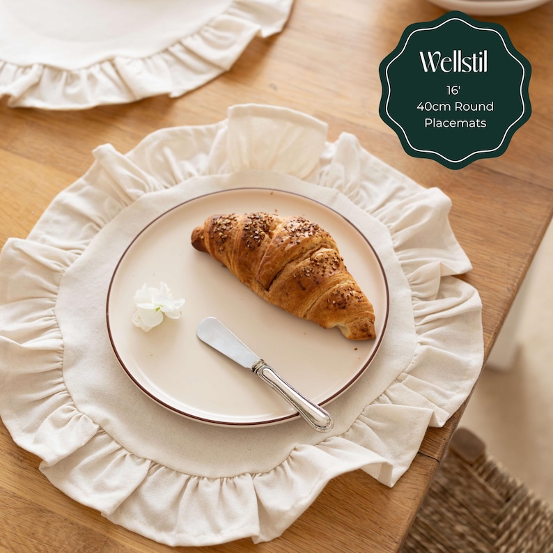 May include: Beige round placemat with a ruffled edge, a plate with a croissant, and a butter knife. The plate is on a wooden table. The placemat is 16 inches or 40cm in diameter. The text on the image says "Wellstil 16" 40cm Round Placemats."