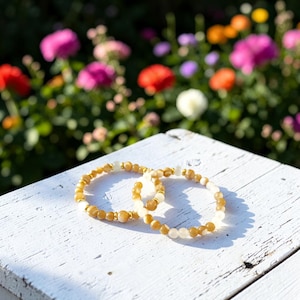 May include: Two beaded bracelets featuring alternating round yellow and translucent white beads. The bracelets are accented with small, polished gold-toned metal spacers placed at regular intervals throughout the circular beaded strands.