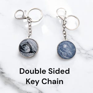 May include: Double-sided keychain with a silver chain and two round, silver-rimmed charms. One charm features a black and white marbled design, and the other charm features a blue and white marbled design.