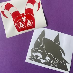 May include: Two vinyl stickers, one red and one gray. The red sticker is a cartoon character with horns and a heart on its chest. The gray sticker is a cartoon character with a long face and large eyes.