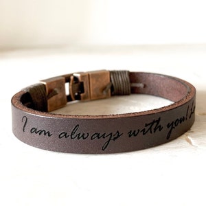 May include: A brown leather bracelet with a metal clasp and the inscription "I am always with you!"