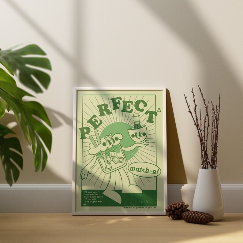 May include: A framed art print with a retro-style illustration in shades of green. The artwork features a cartoon character holding a matcha drink and a bottle. Text includes "PERFECT" and "match-a!" along with a recipe. The print is displayed on a wooden floor.