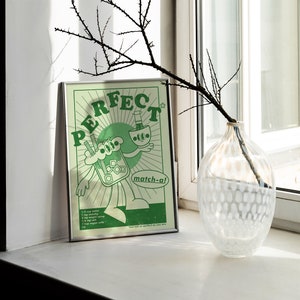 May include: A framed green and white poster with the word "PERFECT" in large letters. The poster features a cartoon illustration of a matcha drink and a bottle, with the text "match-a!" and a recipe at the bottom.
