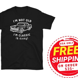 K&ouml;nnte beinhalten: Schwarzes T-Shirt mit wei&szlig;em Text, der "I'm not old I'm classic (& Kinky)" lautet, und einer Illustration eines Oldtimers. Der Text "USA Only Free Shipping on orders $35+" befindet sich auf einem roten Kreis mit wei&szlig;em Rand.