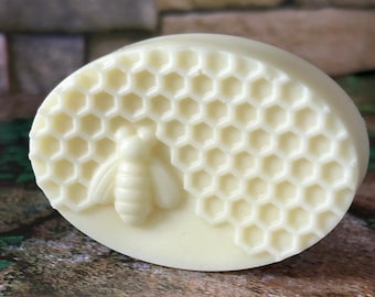 May include: A white oval-shaped soap bar with a honeycomb design and a bee embossed on the side.