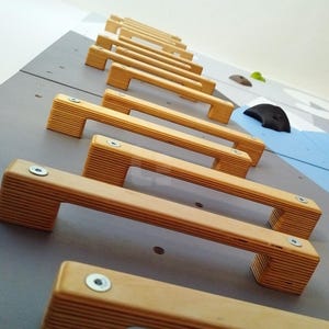 K&ouml;nnte beinhalten: Nahaufnahme einer Kletterwand mit Holzgriffen. Die Griffe sind versetzt angeordnet und aus hellem Holz gefertigt. Die Wand ist hellgrau gestrichen.