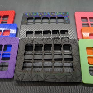 May include: A collection of colorful, rectangular panels with a grid of square cutouts. The panels are in various colors, including red, blue, purple, pink, green, and orange. Some panels have patterned surfaces, such as carbon fiber or a geometric design.