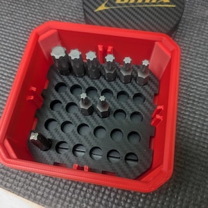 May include: A red plastic storage box with a black carbon fiber pattern insert. The box is filled with a variety of small metal bits.