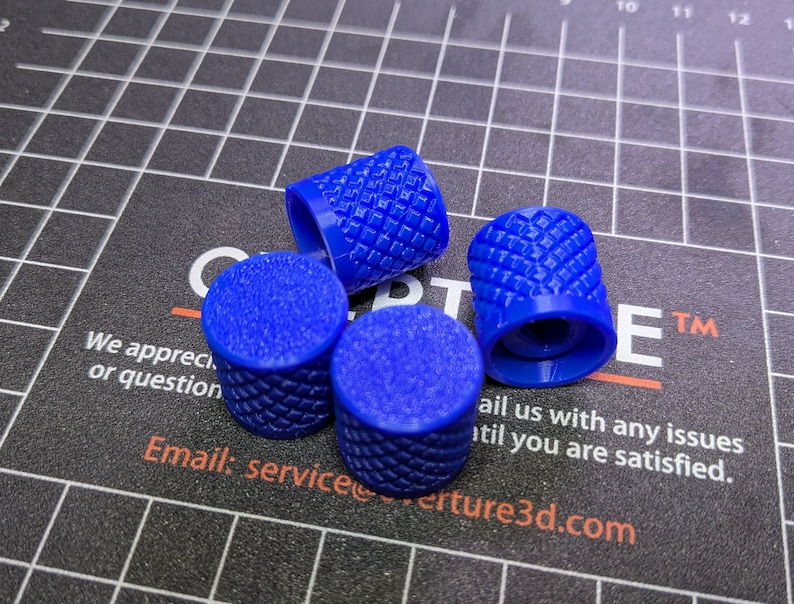 May include: Four blue, textured knobs with a diamond pattern are arranged on a black surface with a grid pattern. The knobs are cylindrical with a slightly domed top. The background includes text and a logo.