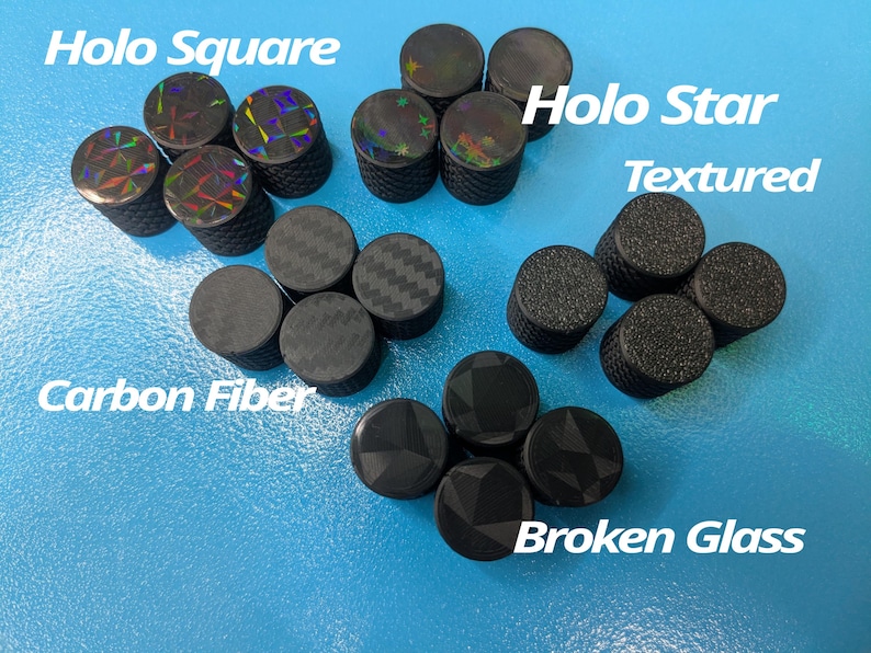 May include: An assortment of black tire valve stem caps with various designs, including "Holo Square," "Holo Star," "Textured," "Carbon Fiber," and "Broken Glass." The caps are arranged on a light blue surface.