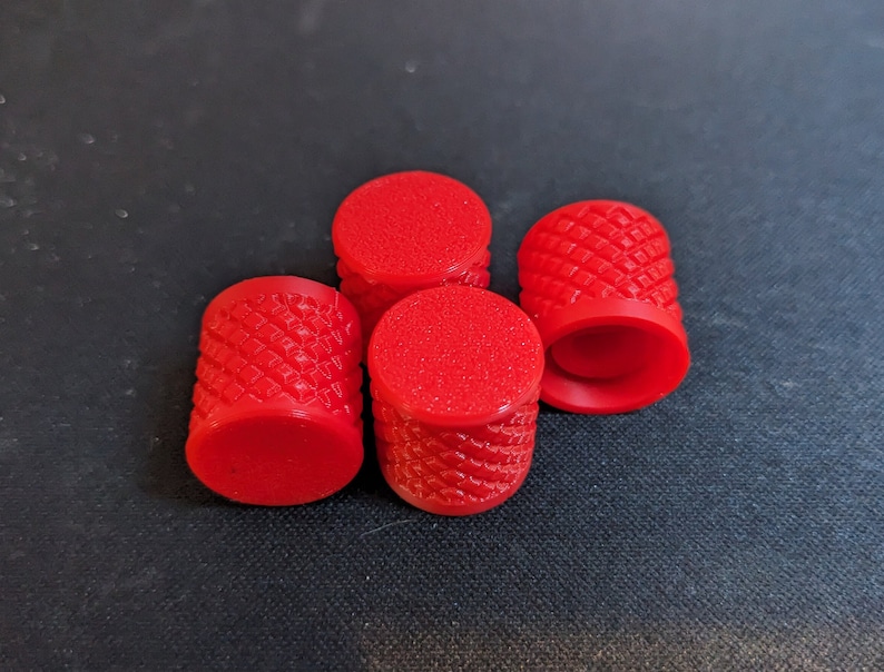 May include: Four bright red, cylindrical objects with textured, diamond-patterned sides and flat tops. One object is hollow, revealing its interior. The objects are arranged on a dark surface.