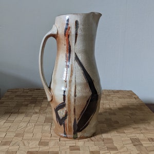 May include: A white ceramic pitcher with brown and black abstract designs. The pitcher has a wide mouth and a handle.