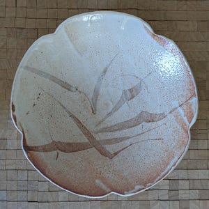 May include: A white ceramic bowl with a scalloped edge and a brown abstract design. The bowl has a speckled glaze.