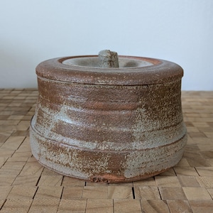 May include: A brown and white ceramic jar with a lid. The jar has a textured surface and a slightly rounded shape. The lid has a small knob on top.