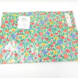 May include: A package of floral fabric featuring a vibrant pattern of red, orange, yellow, and purple flowers on a green background. The fabric is wrapped in clear plastic. A tag with text is visible.