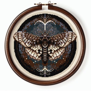 May include: A cross-stitch pattern featuring a brown and white moth with intricate details, set against a dark background with a circular design.