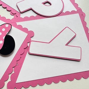 May include: Pink and white banner with scalloped edges and the letters "P" and "Y" in white. The banner is decorated with a black and white polka dot bow.