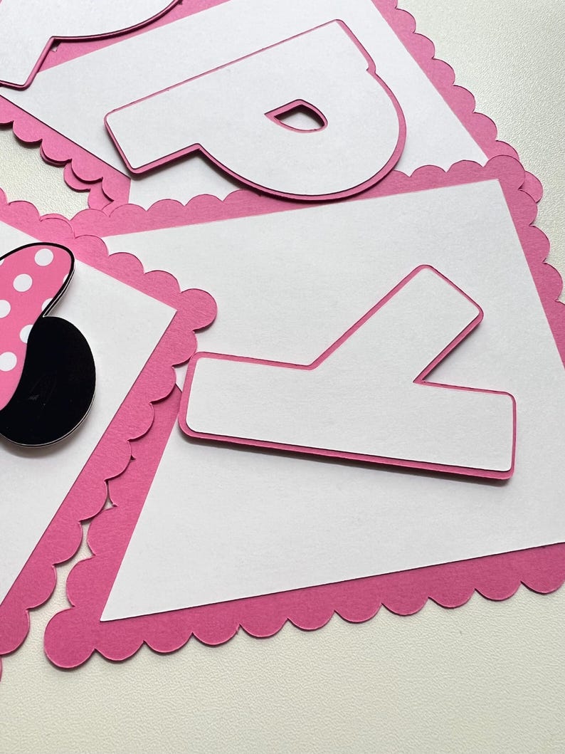 May include: Pink and white banner with scalloped edges and the letters "P" and "Y" in white. The banner is decorated with a black and white polka dot bow.
