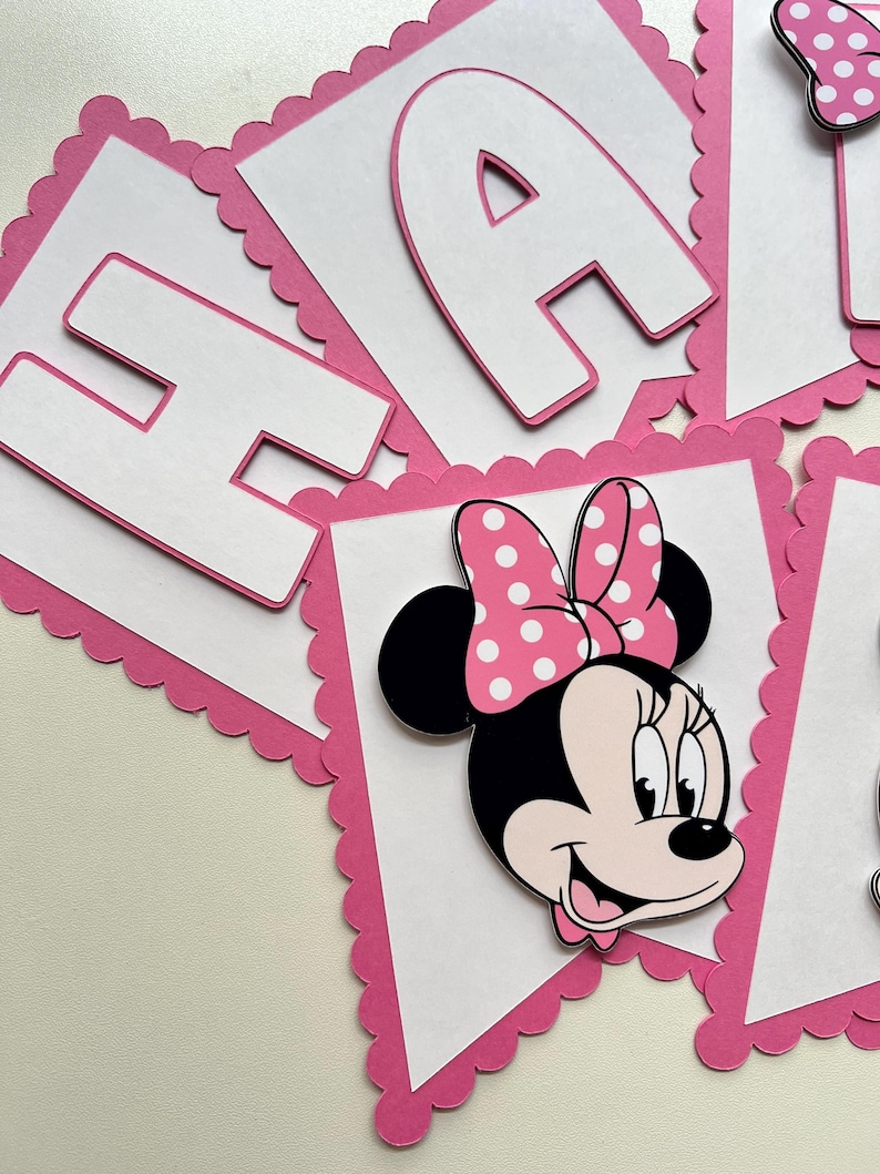 May include: Pink and white banner with scalloped edges featuring the letters "Happy" and a Minnie Mouse character with a red bow and white polka dots.