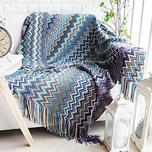 May include: A blue and brown chevron patterned throw blanket with fringe. The blanket is draped over a white sofa.