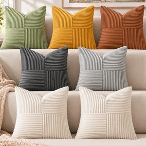 May include: A collection of seven square throw cushions featuring a textured corduroy fabric with a geometric pattern of alternating vertical and horizontal stripes. The cushions are available in sage green, mustard yellow, rust orange, dark grey, light grey, and cream.