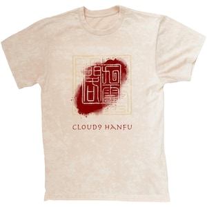 Puede incluir: Una camiseta beige con un gráfico rojo y dorado de un carácter chino y el texto "CLOUD9 HANFU".