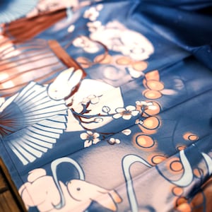 May include: A blue fabric with a white rabbit and a fan design. The fabric has a light blue and white floral pattern with orange circles.