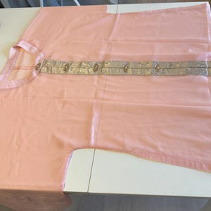 May include: A light pink shirt featuring a mandarin collar and a vertical center panel in a metallic silver fabric. The silver panel is decorated with five small, circular, ornate buttons arranged in a straight line down the front center.