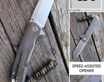 Hoja de acero VG10. Cachas de aleación de titanio anodizadas con efecto cristal de hielo. Navaja EDC. Bloqueo Liner Lock Tanto. Cordón con perla Mando. Aprobada por Odin.