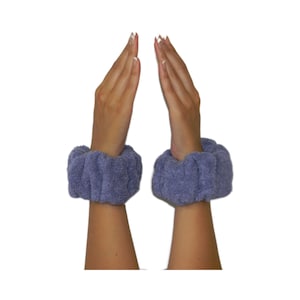 May include: A pair of lavender-colored terrycloth wrist warmers. The warmers are worn on the wrists of a person with their hands raised in a prayer position.