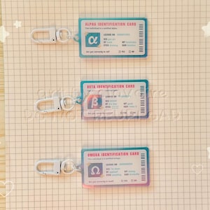 May include: Three clear plastic ID cards with silver keychains. Each card has a different Greek letter: Alpha, Beta, and Omega. The cards have a blue border and include text such as "Identification Card" and "License No."