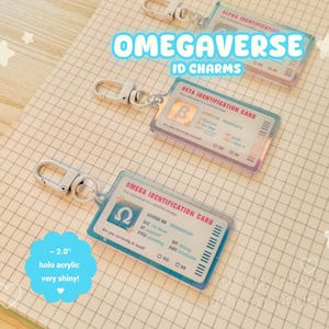 Pode incluir: Pingentes de identificação em acrílico holográfico com fechos prateados. Os pingentes apresentam o texto "OMEGAVERSE ID CHARMS" e incluem designs de "ALPHA", "BETA" e "OMEGA IDENTIFICATION CARD". Cada pingente tem aproximadamente 5 cm e é muito brilhante.