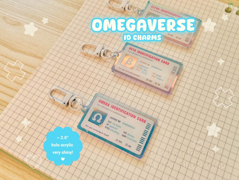 May include: Holographic acrylic ID charms with silver clasps. The charms feature the text "OMEGAVERSE ID CHARMS" and include "ALPHA", "BETA", and "OMEGA IDENTIFICATION CARD" designs. Each charm is approximately 2.0 inches and very shiny.