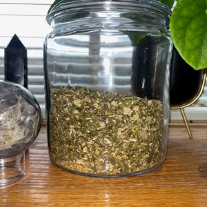 May include: A glass jar with a lid filled with dried herbs and spices. The jar is sitting on a wooden surface.