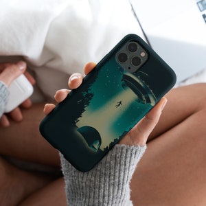 Puede incluir: Una funda de teléfono negra con un gráfico de un platillo volante y una persona cayendo del cielo. El fondo es azul oscuro con estrellas.