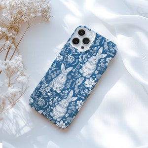 May include: A blue phone case with a white floral pattern and bunnies. The case has a camera lens cutout.