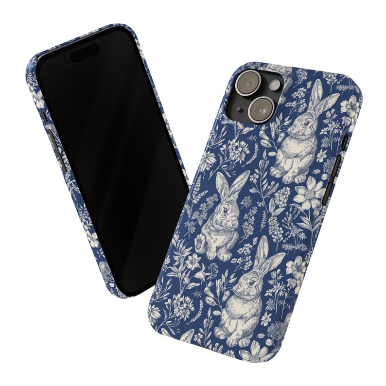 May include: A blue phone case with a white floral pattern and bunnies. The case has a camera cutout and a white background.