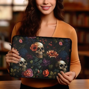 May include: A black laptop sleeve featuring a floral and skull design. The artwork includes skulls, roses, and other flowers in shades of orange, pink, and purple against a dark background. The sleeve has a zipper closure.