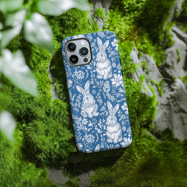 May include: A blue phone case with a white floral pattern and bunnies. The case has a camera lens cutout.