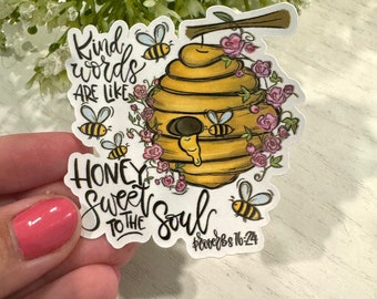 May include: A yellow and brown beehive with pink flowers and bees. The text reads "Kind words are like honey sweet to the soul" and "Proverbs 16:24".