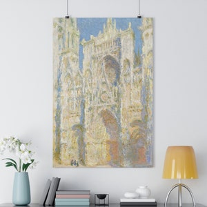 Puede incluir: Una pintura de una gran catedral de piedra blanca con detalles intrincados. La catedral está pintada en un estilo impresionista ligero con colores suaves y pinceladas. La pintura está enmarcada y colgada en una pared blanca.